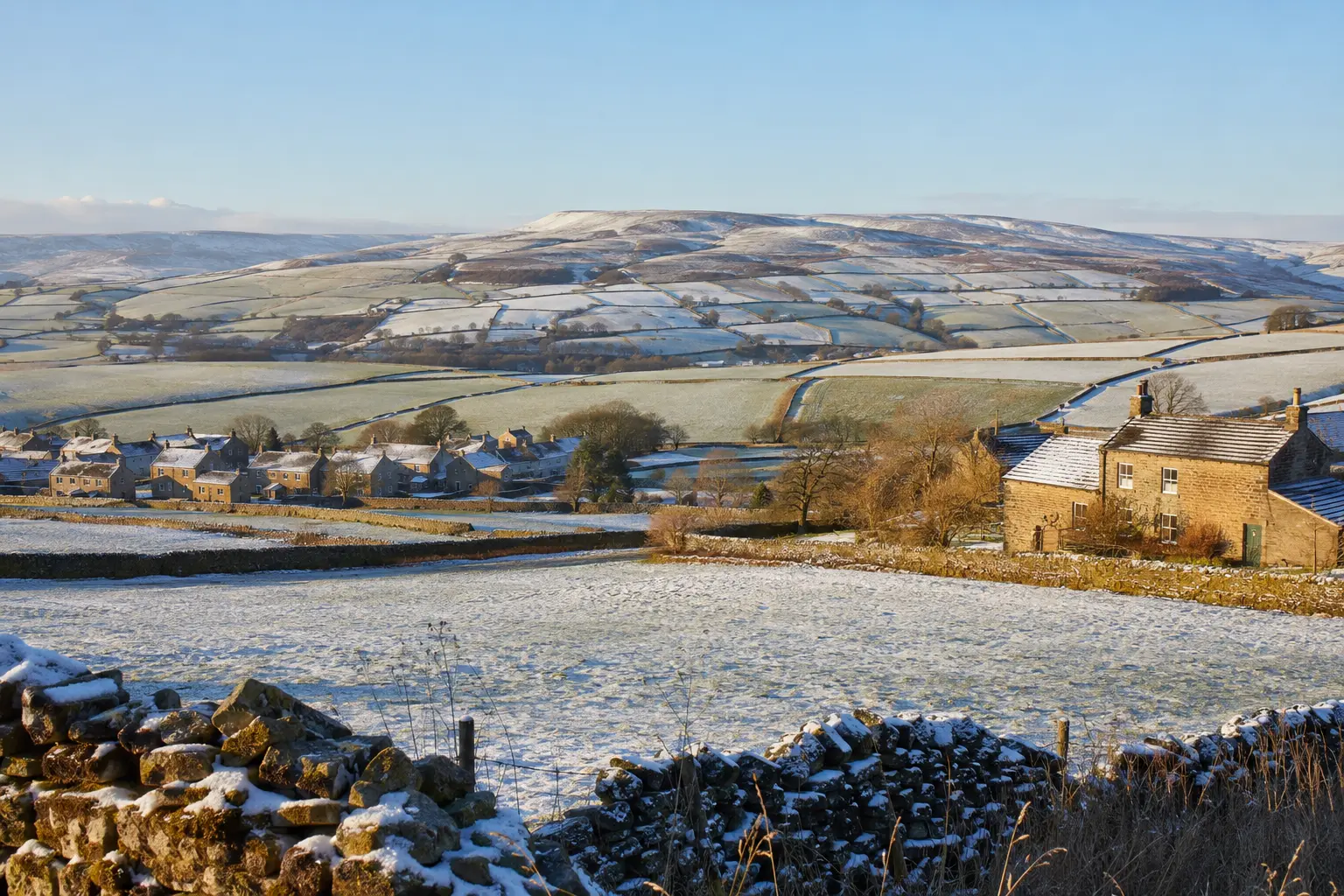 A North Yorkshire stone village and fields under light winter snow and blue sky